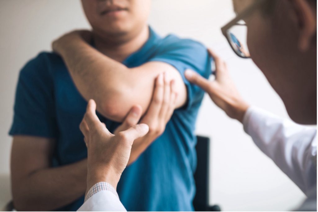 Doctor examining a patient's elbow as their arm is raised across the body.